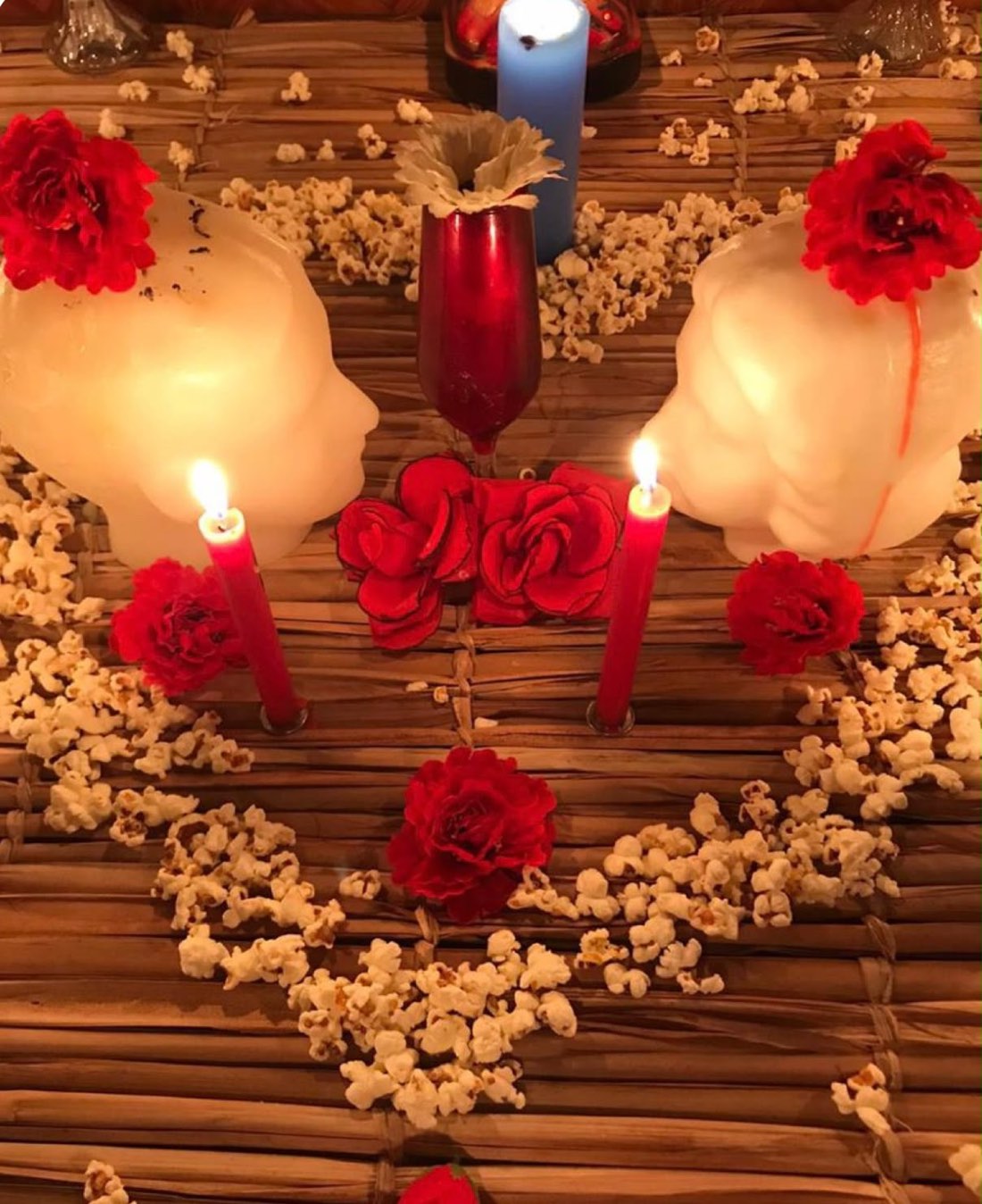 Trabalho de amarração amorosa montado por Yasmin: duas velas em formato de rosto, velas vermelhas, rosas e pipoca sobre esteira